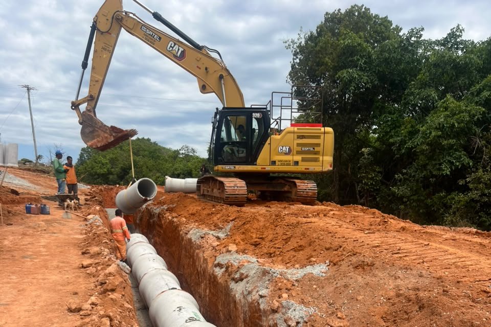Escavadeira assentando tubos em obra de drenagem